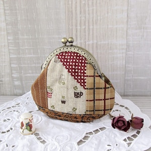 Può includere: Un porta monete in tessuto patchwork marrone e beige con una chiusura in metallo argentato. Il porta monete è decorato con un tessuto a pois rosso e bianco, un tessuto a quadri e un tessuto con un motivo floreale.