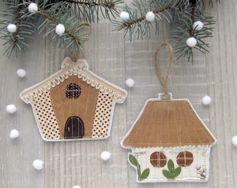 May include: Two handmade felt Christmas ornaments shaped like houses. The houses are brown with white trim and have small windows. The ornaments are hanging from twine.
