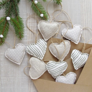 Puede incluir: Una colecci&oacute;n de adornos hechos a mano en forma de coraz&oacute;n en un sobre marr&oacute;n. Los adornos est&aacute;n hechos de tela y presentan diferentes patrones, incluyendo lunares, rayas y una textura de lino lisa. Los adornos son de color beige claro con acentos grises.