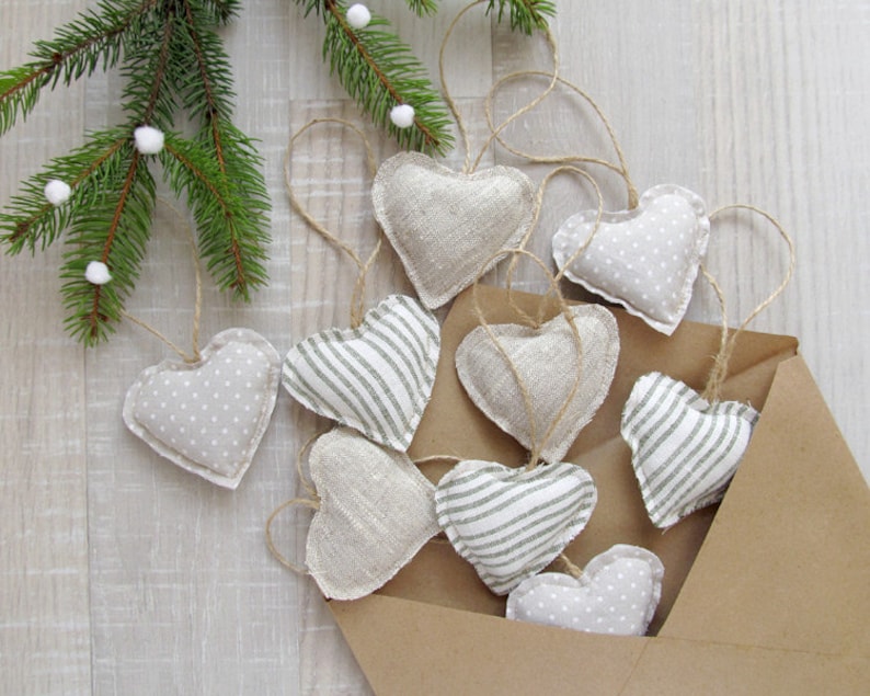 Puede incluir: Una colecci&oacute;n de adornos hechos a mano en forma de coraz&oacute;n en un sobre marr&oacute;n. Los adornos est&aacute;n hechos de tela y presentan diferentes patrones, incluyendo lunares, rayas y una textura de lino lisa. Los adornos son de color beige claro con acentos grises.