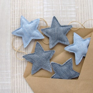 May include: Five blue denim star-shaped ornaments with a brown paper envelope background. The stars are sewn together with twine.