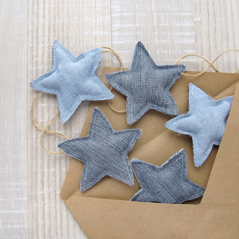 May include: Five blue denim star-shaped ornaments with a brown paper envelope background. The stars are sewn together with twine.