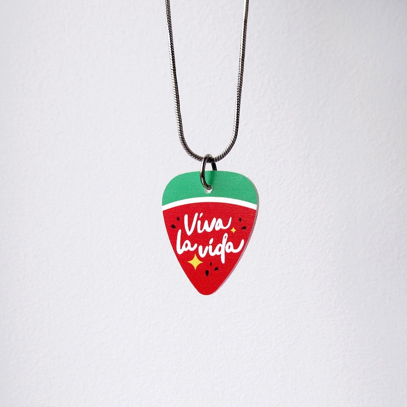 May include: A guitar pick pendant necklace with a red and green watermelon design. The pendant has the words "Viva la vida" in white script, with a yellow star accent. The necklace chain is silver.