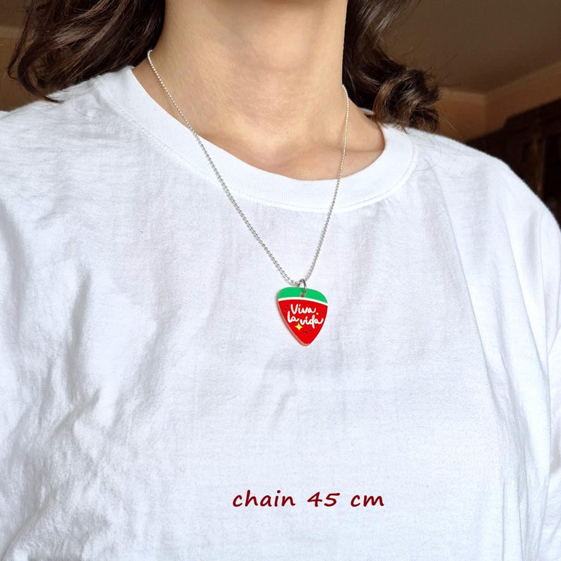 May include: A silver chain necklace with a strawberry pendant. The pendant is red with a green top and the words "Viva la vida" in white. The chain is 17.7 inches long.