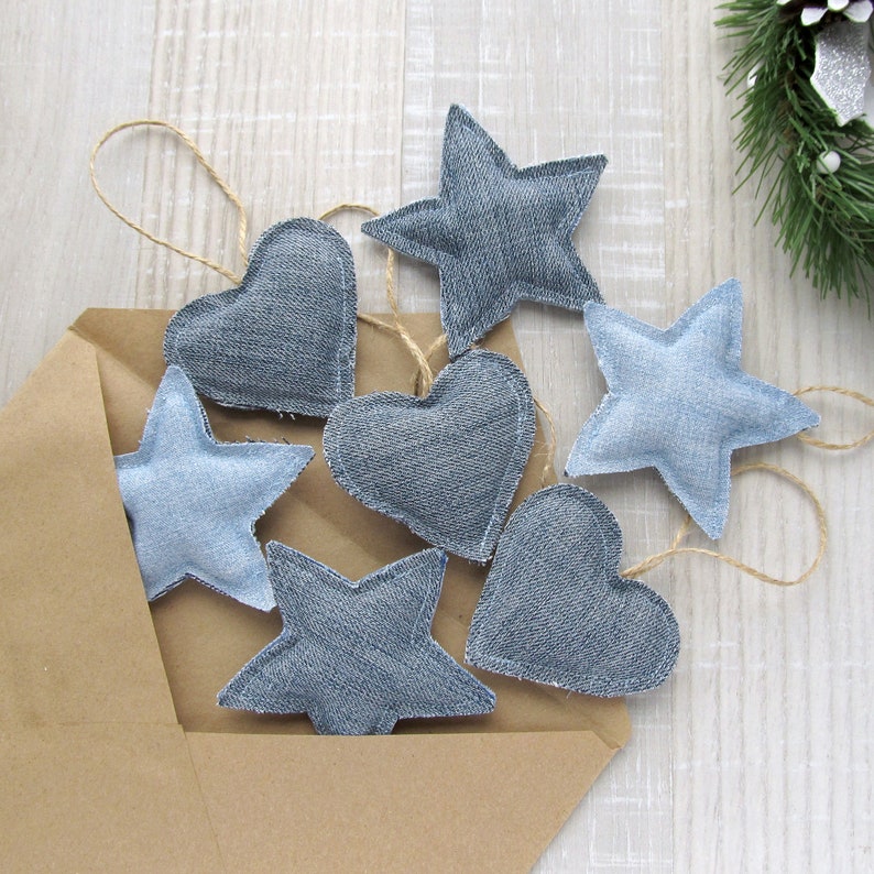May include: A brown paper envelope filled with blue denim heart and star ornaments. The ornaments are tied with twine and are ready to be hung on a Christmas tree.