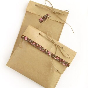 Op de afbeelding: Twee bruine papieren cadeauzakjes met touwtjes. E&eacute;n zakje heeft een bloemenlint en het andere heeft een klein bloemetjeslabel.