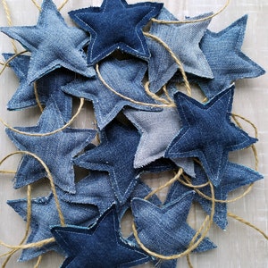 May include: A garland of denim stars strung together with twine. The stars are various shades of blue and are sewn together with a contrasting thread.