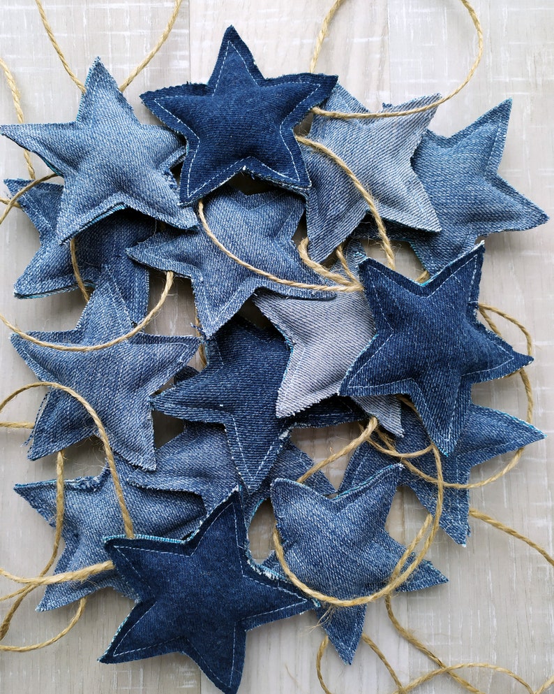 May include: A garland of denim stars strung together with twine. The stars are various shades of blue and are sewn together with a contrasting thread.