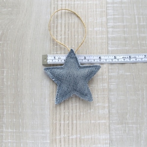 May include: A blue denim star ornament with a brown twine hanger. The star is approximately 4 inches wide.