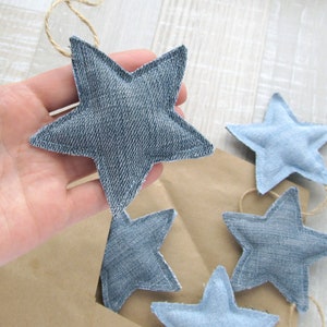 May include: A garland of five denim stars, each with a different shade of blue, is strung together with twine. The stars are hanging on a brown paper background.