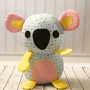 May include: A blue and pink koala plush toy with yellow accents. The koala has a patterned fabric body and a black nose.