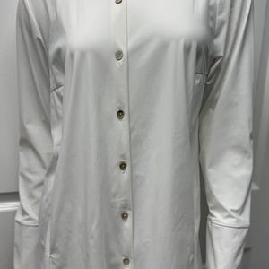 May include: A long-sleeved, white button-down shirt with a classic collar. The shirt features a tailored fit and is fastened with six pearlescent buttons. The cuffs are finished with a simple, clean design. The shirt is made of a smooth, wrinkle-resistant fabric.