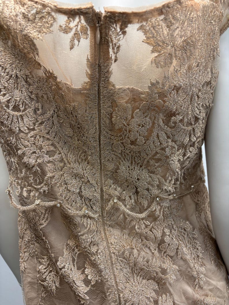 Pode incluir: Um vestido de renda bege com fecho de z&iacute;per nas costas. O vestido tem um delicado padr&atilde;o floral e uma bainha festonada.