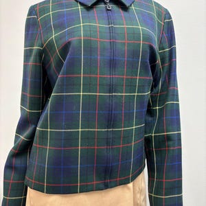 May include: A green, blue, red, and yellow plaid jacket with a zip-up front and a collar. The jacket is displayed on a mannequin. The jacket's pattern is a classic tartan design.