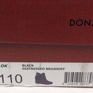 May include: A close-up of a shoe box with the brand name "DONALD/F" in black text on a dark red background. The box label reads "LULUU-DK" and "BLACK DISTRESSED BRUSHOFF". A silhouette of a black boot is also on the label.