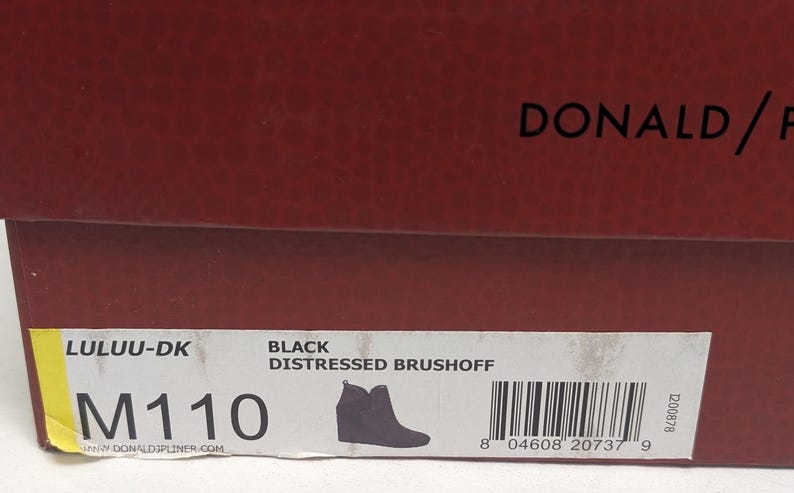 May include: A close-up of a shoe box with the brand name "DONALD/F" in black text on a dark red background. The box label reads "LULUU-DK" and "BLACK DISTRESSED BRUSHOFF". A silhouette of a black boot is also on the label.