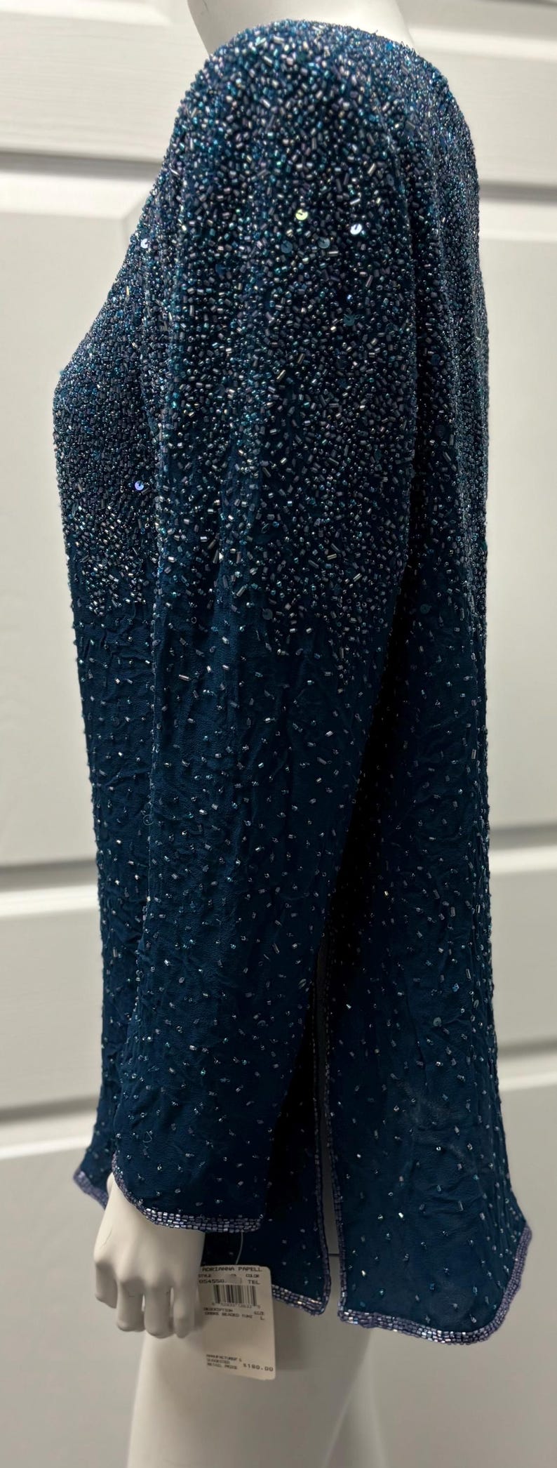 May include: A long-sleeved, dark teal beaded top. The garment is covered in small, shimmering beads that create a textured effect. The beads are densely packed at the top and gradually become less dense towards the bottom.