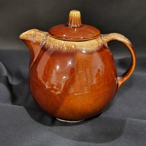 May include: A brown ceramic teapot with a rounded body and a lid with a knob on top. The teapot has a brown glaze with a speckled pattern.