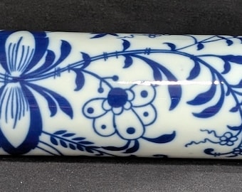 May include: A rolling pin with a white ceramic barrel featuring a blue floral design. The wooden handles are light brown. This kitchen tool is designed for rolling out dough.