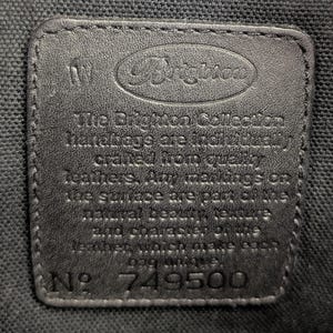 May include: A close-up of a black leather tag with the Brighton logo embossed at the top. The tag includes the text "The Brighton Collection handbags are individually crafted from quality leathers. Any markings on the surface are part of the natural beauty..." and the number 749500.