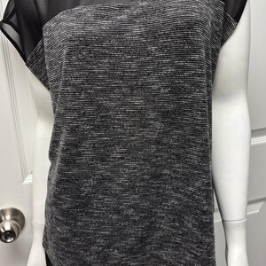 May include: A black and gray top with a sheer black yoke and short sleeves. The body of the top is a textured gray knit fabric. The bottom of the top has a black, flowing, sheer fabric.