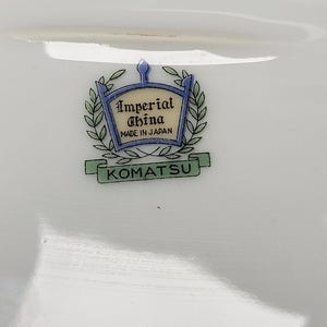 May include: White porcelain dish with the text "Imperial China MADE IN JAPAN" and the name "KOMATSU" in a green banner. The logo is framed by a blue and gold crest with laurel leaves.