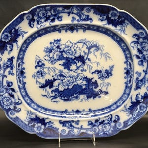 May include: A white ceramic mug with a black handle and the text "But First, Coffee" in a black, handwritten-style font. The mug is on a white surface.