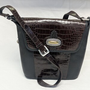 May include: A brown and black leather crossbody bag with a crocodile-textured flap and accents. The bag features a silver buckle and a decorative clasp with gold and silver details. The adjustable strap is also brown leather.