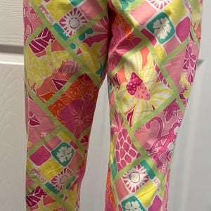 May include: Pink, yellow, and green patterned pants. The pants feature a repeating geometric design with floral and abstract shapes. The colors are vibrant and the overall style is casual. The pants are displayed on a mannequin.