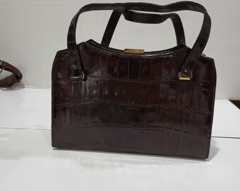 May include: A dark brown crocodile embossed leather handbag with a top clasp closure and two top handles.