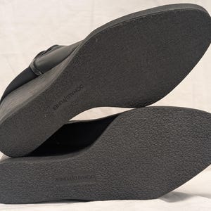 May include: Black wedge-heeled shoes with textured soles. The soles are marked with the brand name "DONALD J PLINER". The shoes have a sleek, modern design, suitable for various occasions.