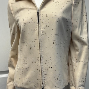 May include: Cream-colored jacket with a perforated dot pattern. The jacket features a full-length zipper, a collared neckline, and long sleeves. The garment has a tailored fit and a small pocket on the left side.