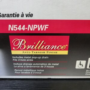 May include: A red and black box with the text "Garantie &agrave; vie" and "N544-NPWF" on the top. The box also features the text "Brilliance Anti-Tarnish Finish" and includes details about the product's features, such as a metal pop-up drain and a 3-hole sink.