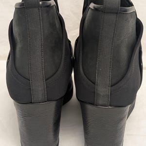May include: A pair of black ankle boots with wedge heels. The boots have a sleek, modern design with a combination of smooth and textured materials. The heels are approximately 3 inches high, providing a stylish lift.