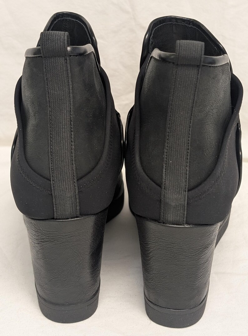 May include: A pair of black ankle boots with wedge heels. The boots have a sleek, modern design with a combination of smooth and textured materials. The heels are approximately 3 inches high, providing a stylish lift.