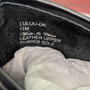May include: Close-up of the inside of a black shoe. The text "LULU-DK 11M Made In China LEATHER UPPER RUBBER SOLE" is visible. The shoe's interior is black, and white tissue paper is inside.
