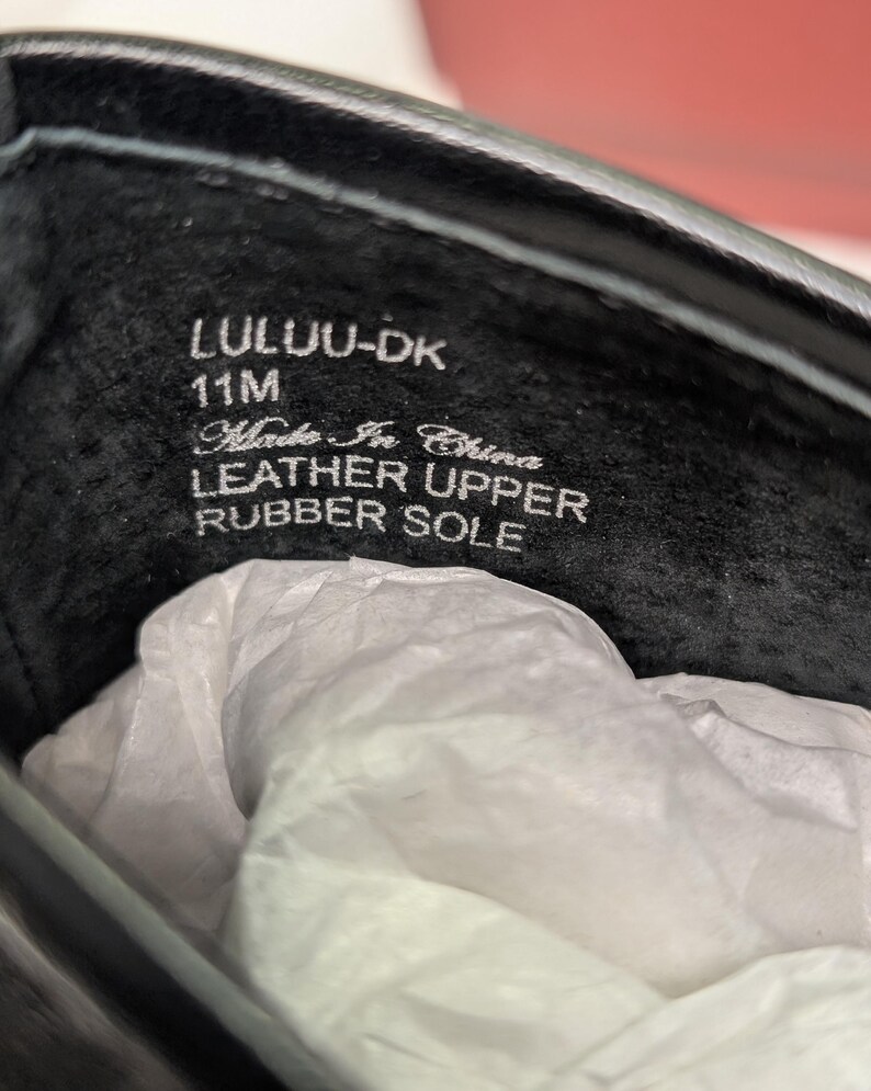 May include: Close-up of the inside of a black shoe. The text "LULU-DK 11M Made In China LEATHER UPPER RUBBER SOLE" is visible. The shoe's interior is black, and white tissue paper is inside.