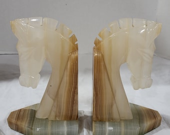 May include: A pair of bookends made of white and brown marble, shaped like horse heads. The bookends have a green marble base.