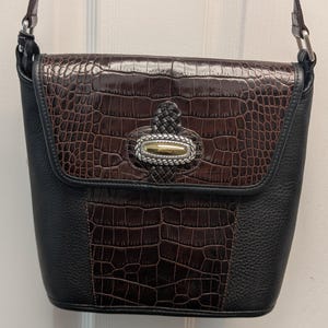 May include: A black and brown crossbody bag with a flap closure. The flap and center panel feature a faux crocodile skin texture in brown. The bag has a silver and gold-toned clasp and a braided leather handle.