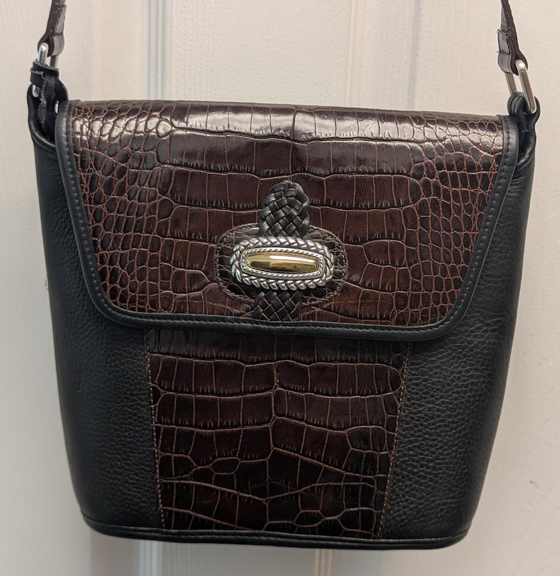 May include: A black and brown crossbody bag with a flap closure. The flap and center panel feature a faux crocodile skin texture in brown. The bag has a silver and gold-toned clasp and a braided leather handle.