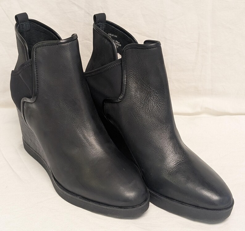 May include: A pair of black leather wedge ankle boots. The boots have a sleek design with a rounded toe, elastic side panels, and a wedge heel. The boots are made of smooth leather and have a rubber sole.