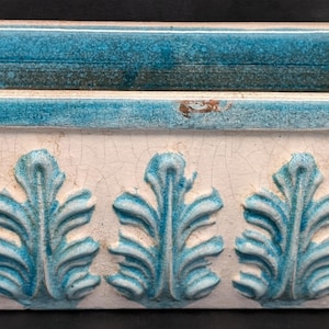 May include: Rectangular ceramic planter with a turquoise interior and trim. The exterior is off-white with a crackle finish and turquoise leaf designs. A decorative container for plants.