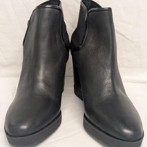 May include: A pair of black leather ankle boots with a rounded toe and a block heel. The boots have a platform sole and elastic side panels. The heel height is approximately 3 inches.