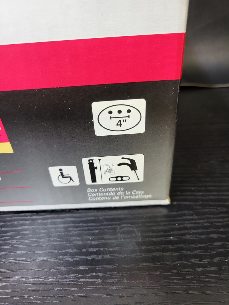 May include: A black and white illustration of a wheelchair, a faucet, and a pipe wrench. The text "Box Contents, Contenido de la Caja, Contenu de l'emballage" is printed below the illustrations.