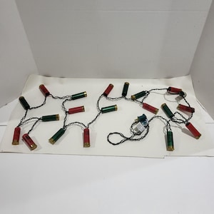 May include: A string of Christmas lights with red and green shotgun shell-shaped bulbs. The lights are strung on a black wire and have a plug on one end.