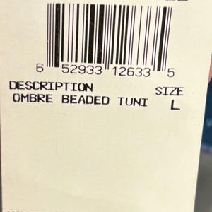May include: A white tag with the text "ADRIANNA PAPELL" and a barcode. The tag also includes the style number "054550720", the description "OMBRE BEADED TUNI", and the size "L".