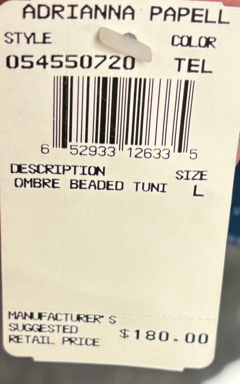 May include: A white tag with the text "ADRIANNA PAPELL" and a barcode. The tag also includes the style number "054550720", the description "OMBRE BEADED TUNI", and the size "L".