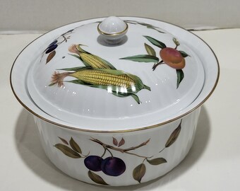May include: White ceramic serving dish with lid, featuring a gold rim and a decorative fruit and vegetable design. The lid is adorned with illustrations of corn, peaches, and plums. A small, round knob tops the lid.