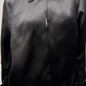 May include: A black satin blouse with a classic collar and long sleeves. The blouse has a buttoned cuff detail and a subtle sheen. The top is a solid black color, offering a sleek and versatile look. The blouse is a stylish addition to any wardrobe.