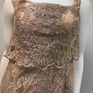 Pode incluir: Um vestido sem mangas feito de renda bege delicada com um padr&atilde;o floral. O vestido tem um decote quadrado e uma saia em camadas.